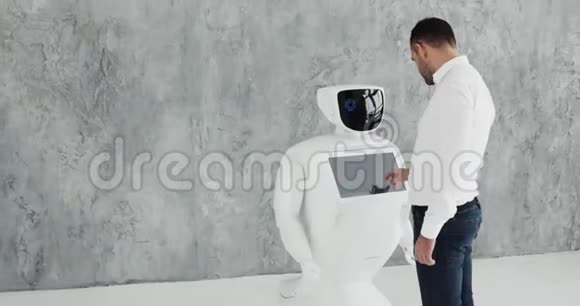 一个时尚的男人与机器人交流把一只塑料机械手臂按在机器人身上握手控制系统视频的预览图