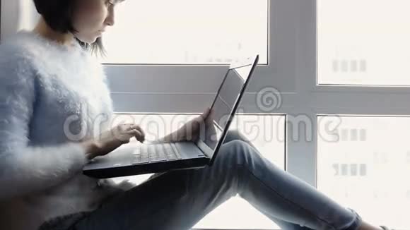 年轻迷人的女孩坐在窗边手里拿着笔记本电脑一位美丽的黑发商界女性在电脑上工作视频的预览图