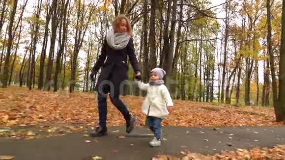 年轻女子和她的孩子在秋天公园散步牵着手慢动作稳定射击视频的预览图