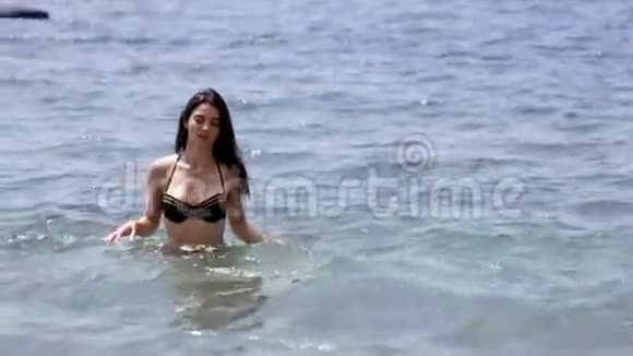 游泳后穿着黑色比基尼从海里出来的迷人年轻女子视频的预览图