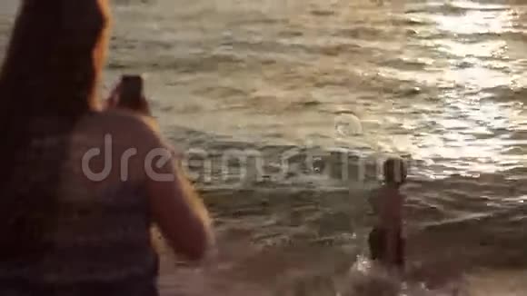 青少年女孩拍照小男孩与移动智能手机相机在海上日落视频的预览图