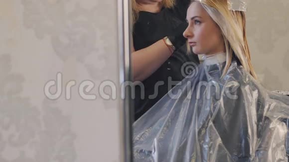 专业染发美容工作室客户椅子上的女孩看着镜子里的倒影视频的预览图