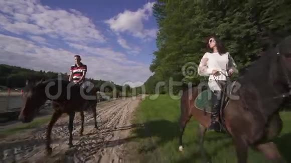 幸福的年轻家庭夫妇一起在河岸骑马蓝天背景视频的预览图