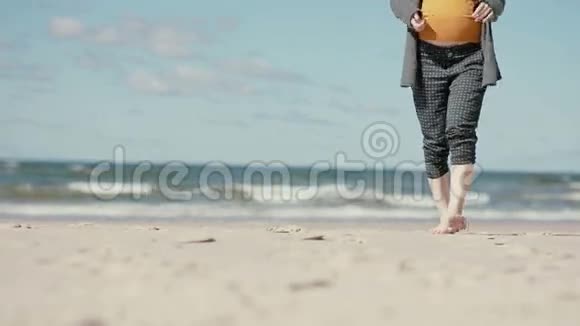 一位孕妇正光着脚在沙滩上慢慢接近镜头视频的预览图