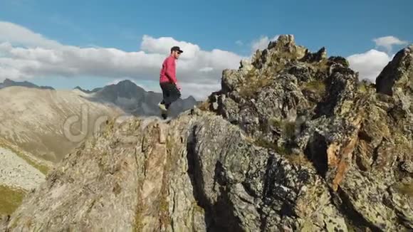 一个留着胡子的年轻人一个戴着帽子和太阳镜的登山者爬上了高山上的一个岩石岭公园游视频的预览图
