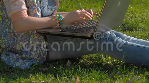 孩子在笔记本电脑上工作一个戴着太阳镜的十几岁的女孩坐在公园的草地上女孩阳光户外视频的预览图