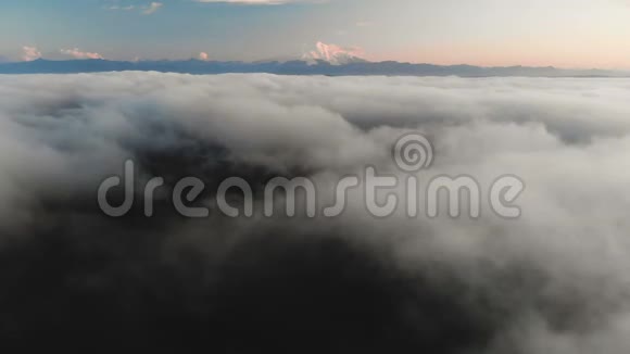 在黄昏或黎明时飞过云层在云层之上朝一座高雪山的方向飞去空中飞行视频的预览图