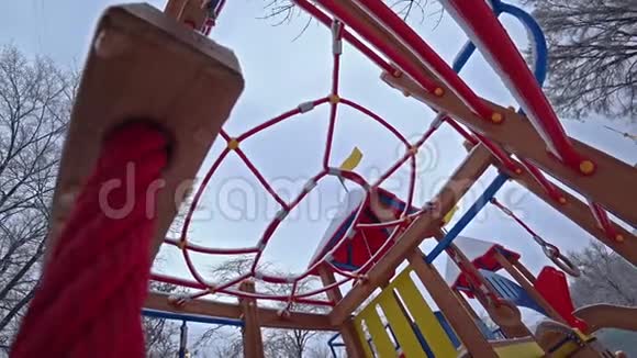 空孩子在阳光明媚的冬日在城市公园的操场上摇摆从底部看背光视频的预览图