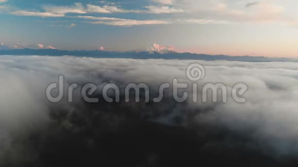在黄昏或黎明时飞过云层在云层之上朝一座高雪山的方向飞去空中飞行视频的预览图