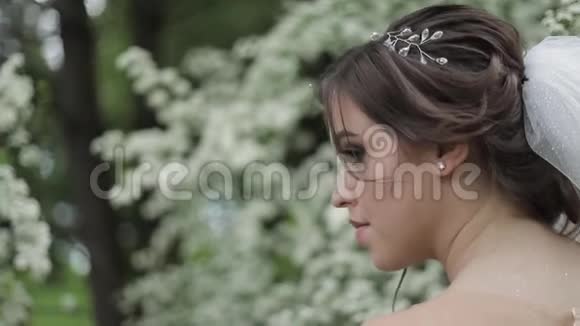 穿着华丽婚纱的迷人新娘捧着花束站在盛开的树木前视频的预览图