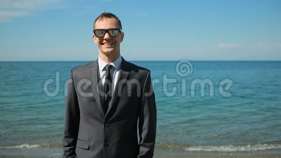 商人穿着西装在海滩上散步承认美丽的海滩他看着摄像机笑了他很高兴视频的预览图