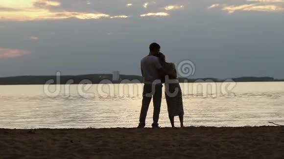 日落时分情人的剪影年轻漂亮的夫妇拥抱在湖岸上视频的预览图
