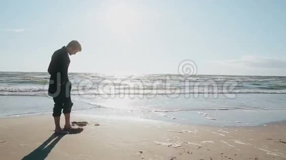 一个年轻人光着脚站在美丽的沙滩上用脚趾在沙滩上挖一个洞视频的预览图