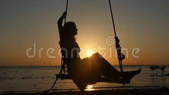 美丽的年轻女子在金色的夕阳下在热带海滩的秋千上摇摆慢动作1920x1080视频的预览图