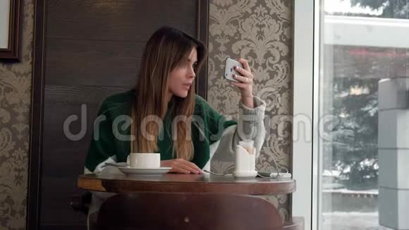 一个漂亮的女孩在咖啡馆喝茶在手机自拍拍照视频的预览图