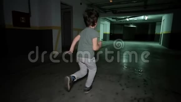 小男孩在地下车库里奔跑孩子在宽敞明亮的停车场周围开车视频的预览图