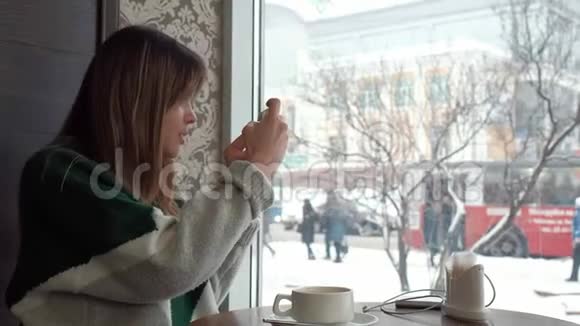 一个漂亮的女孩在咖啡馆喝茶在手机自拍拍照视频的预览图