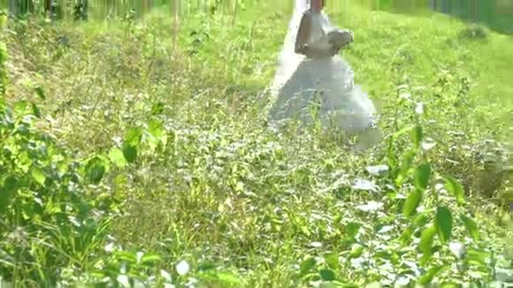 穿着白色连衣裙的漂亮新娘和格罗姆在田野里旋转慢慢地视频的预览图