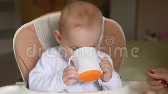 小女孩在儿童座椅上喝水微笑幸福的家庭观念妈妈用勺子和婴儿食品视频的预览图