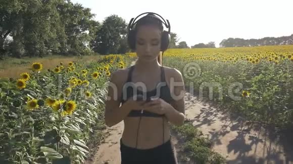 可爱的跑步女孩跑过田野她用耳机听音乐视频的预览图