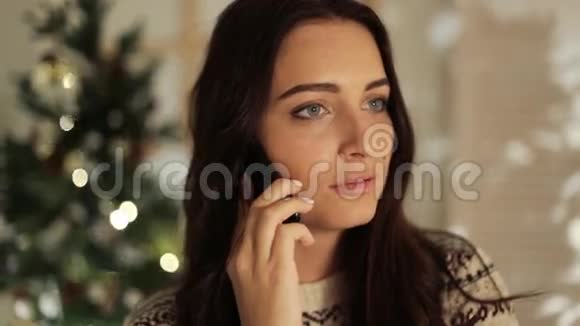 保持联系美丽的年轻微笑的女人穿着白色毛衣在手机上说着轻松的圣诞节视频的预览图