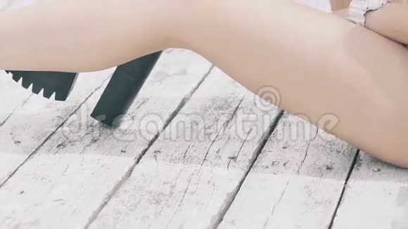 小女孩长腿坐在沙滩户外的木地板上慢慢地视频的预览图