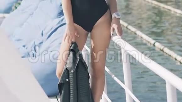 穿着黑色泳衣的女孩拿着皮夹克在海上码头摆姿势慢慢地视频的预览图