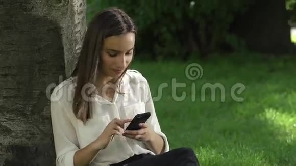 女商人在公园的树下检查手机视频的预览图