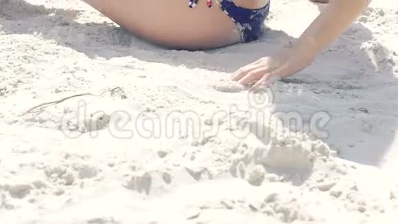 穿泳装的时髦女人在海滩上用腿浇沙慢慢地视频的预览图
