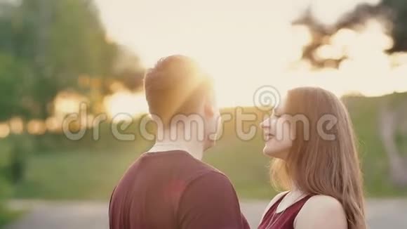 年轻的恋人在日落时站在彼此面前他们微笑男人轻轻抚摸她的头发女人摇动头发慢节奏视频的预览图