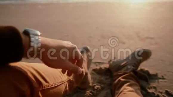 一个男子坐在沙滩上穿着靴子在海上观看美丽日落的视频视频的预览图