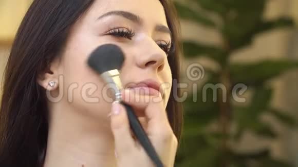专业化妆师将化妆品涂在可爱的少女脸上用于皮肤护理和健康肤色视频的预览图