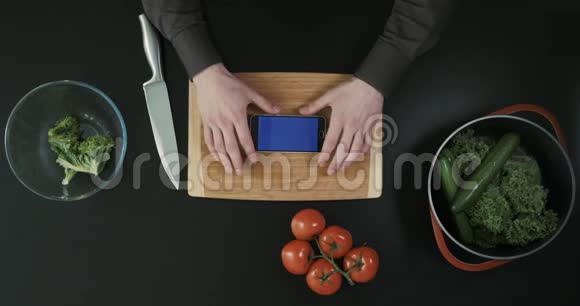 从顶部看手握着电话厨房桌子上有切菜板刀和蔬菜视频的预览图