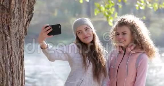 两个漂亮的小女孩在手机上拍照靠近树户外日出早秋公园视频的预览图