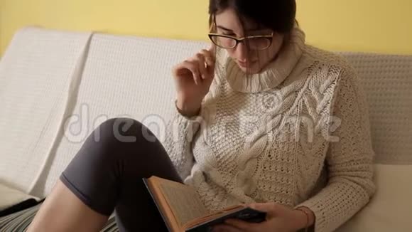 一个穿着白色毛衣的年轻女孩在一个冬天的晚上带着眼镜在家看书书晚上好女孩阅读阅读视频的预览图