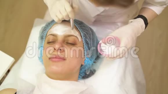 在治疗和按摩后闭上美容师的手在病人的脸上涂上奶油视频的预览图