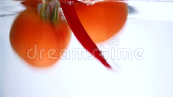 新鲜西红柿和辣椒落入清水中的特写镜头白色背景上有大的水花健康饮食视频的预览图