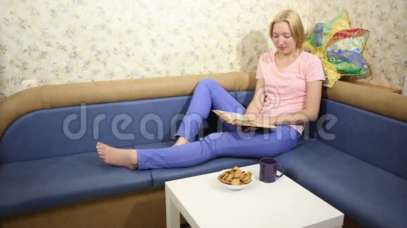年轻女子坐在沙发上看书喝茶视频的预览图