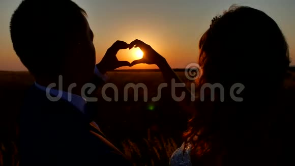 新婚的双手形成一个心形与日落轮廓为太阳准备的手型形成心脏形状的手视频的预览图