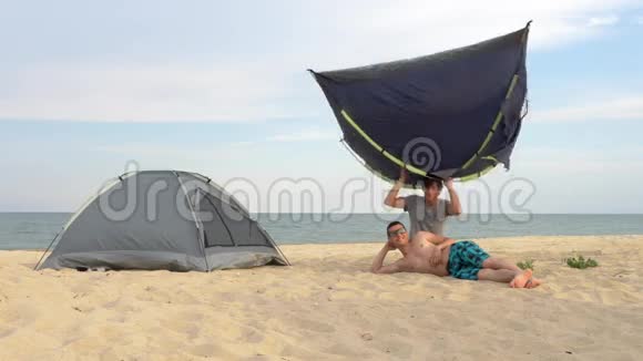 两个人在海滩上玩帐篷在海边的露营地安装帐篷视频的预览图