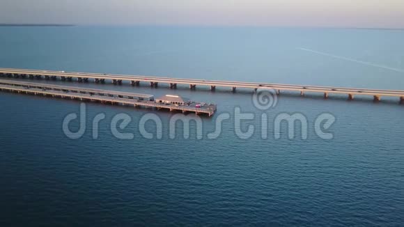夕阳西下温暖的粉红色黄昏越过巨大的公路钢桥穿过平静的蓝海4k空中无人机海景视频的预览图
