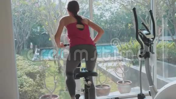 运动的年轻女子骑着运动自行车在健身房慢动作后视视频的预览图