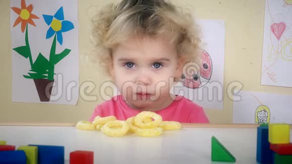 小女孩吃玉米圈坐在她的桌子旁边玩具和图画视频的预览图