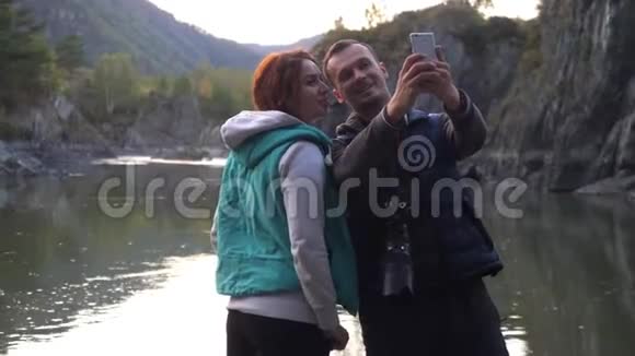 年轻的一对游客在一条山河的背景上自拍通过电话拍照3840x2160视频的预览图
