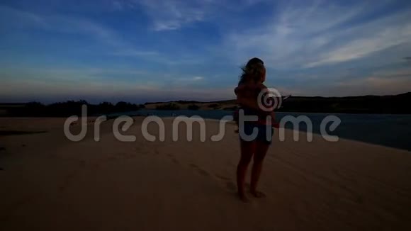 剪影母亲把小女孩抱在怀里在日落的湖边拍照视频的预览图