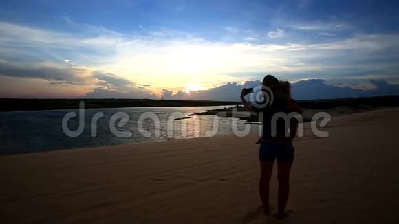 剪影母亲把小女孩抱在怀里在日落的湖边拍照视频的预览图