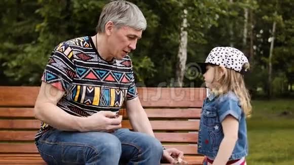 祖父和孙女一起坐在公园长椅上视频的预览图