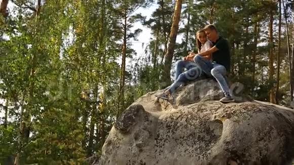 阳光明媚的一天一对年轻夫妇在松树林里的石头上散步视频的预览图