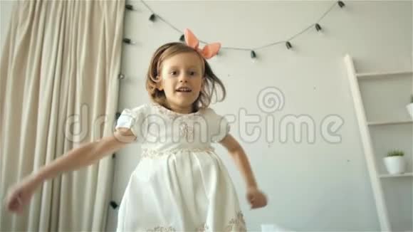 一个快乐可爱的小女孩穿着白色连衣裙在床上蹦蹦跳跳微笑着的小孩子视频的预览图