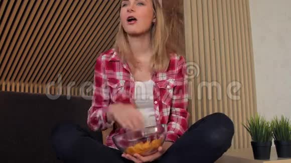 年轻女子在沙发上吃薯片看电视视频的预览图